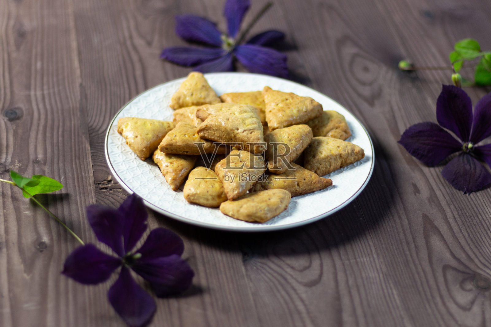 白色盘子上放着蜂蜜饼干，棕色的木质背景上点缀着鲜花照片摄影图片