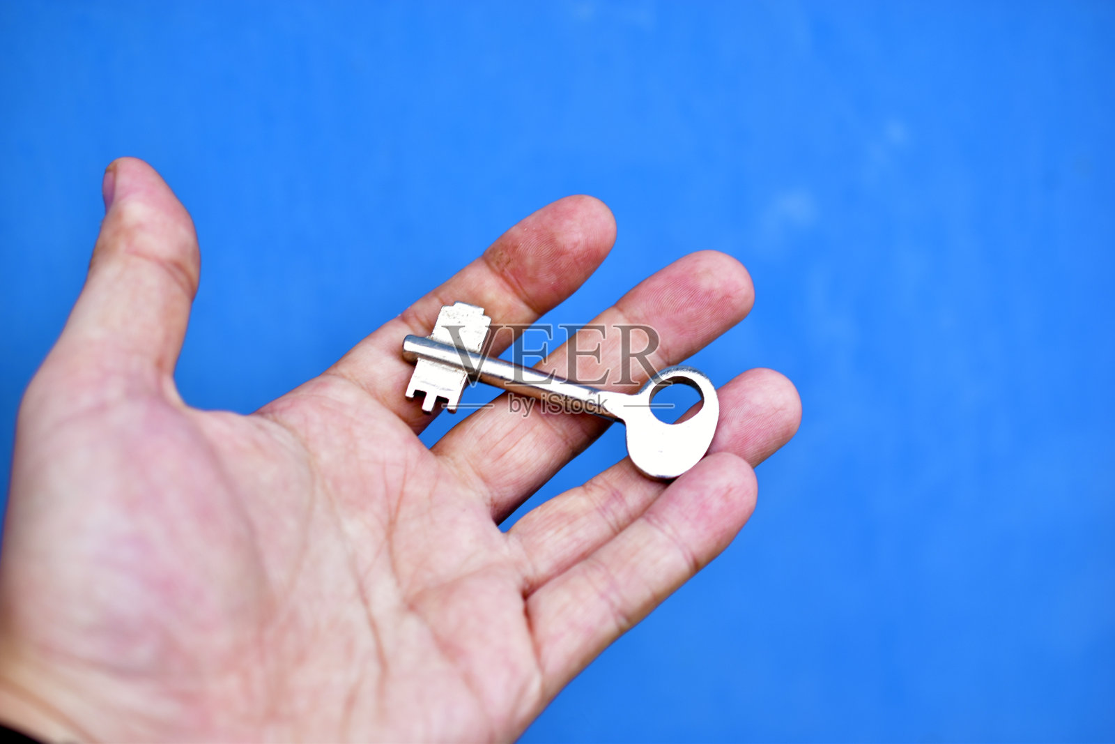 一个蓝色背景的男人手里拿着金属门钥匙照片摄影图片