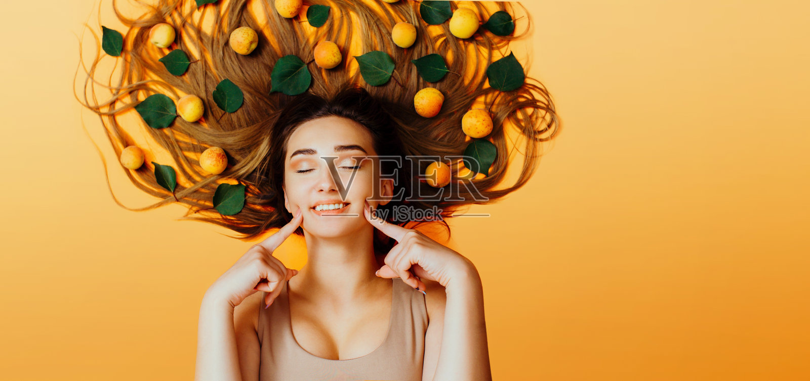 一个美丽的女孩的肖像躺在背景与杏子长头发，概念夏季艺术，年轻女子的脸微笑顶视图照片摄影图片