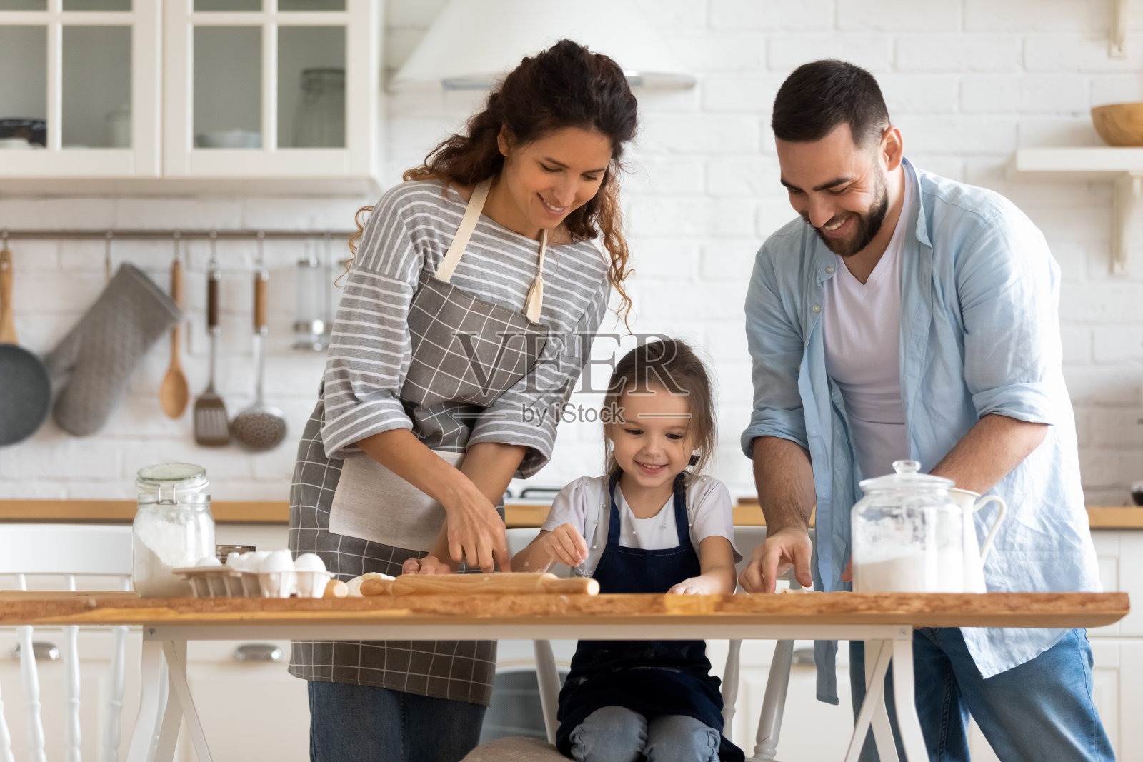 微笑的年轻夫妇教小女儿在厨房烤蛋糕。照片摄影图片