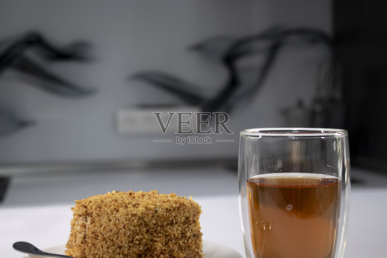 灰色厨房的白色桌子上放着一杯双层杯里的茶和一块蛋糕照片摄影图片