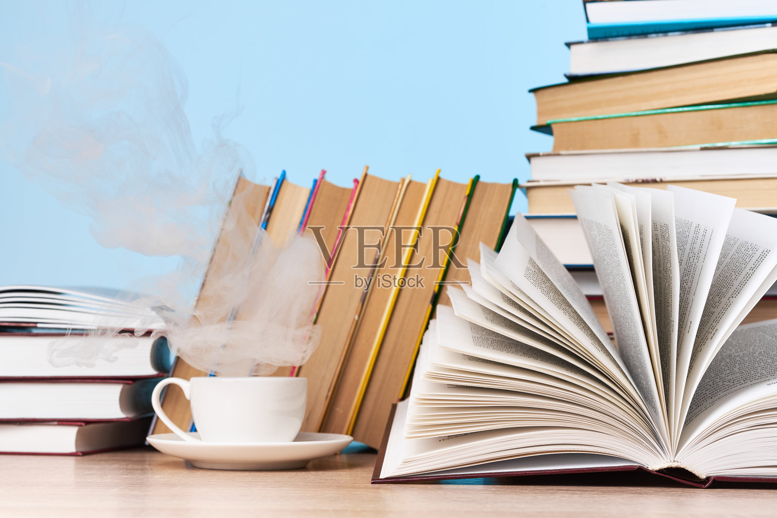 一个打开的书和各种各样的书被放在一个木桌上，靠在浅蓝色的墙壁，这是一个文本的地方照片摄影图片