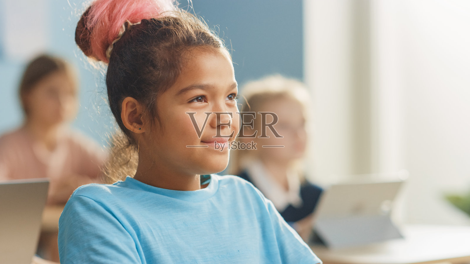 一个可爱的小女孩的肖像与棕色头发微笑迷人，笑着看着老师。照片摄影图片
