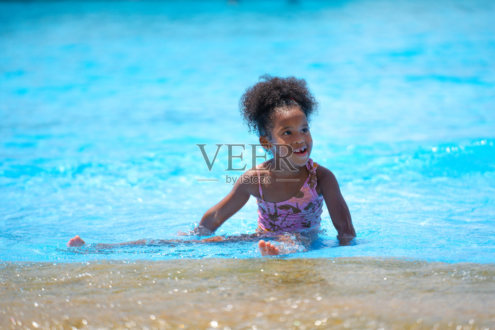 非洲女孩坐在游乐园的游泳池里玩水。概念儿童表达的是纯粹的快乐和兴奋照片摄影图片