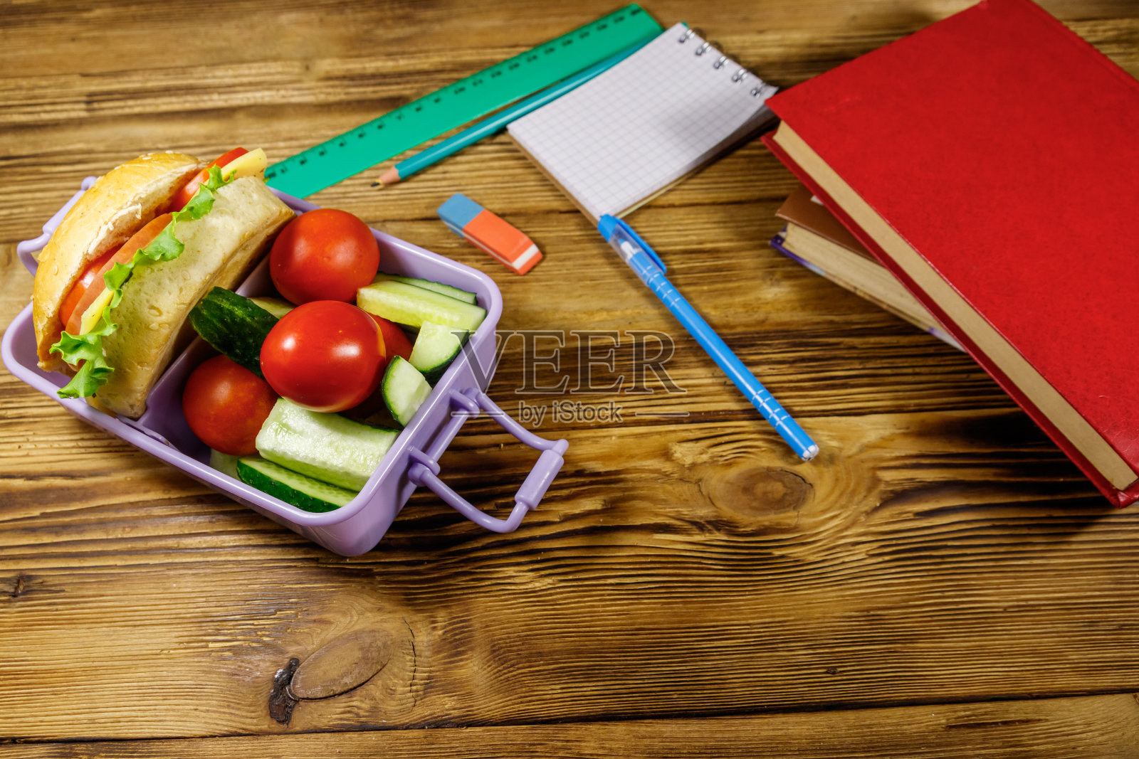 回到学校的概念。木制的桌子上放着学校用品、书籍和装有汉堡和新鲜蔬菜的午餐盒照片摄影图片