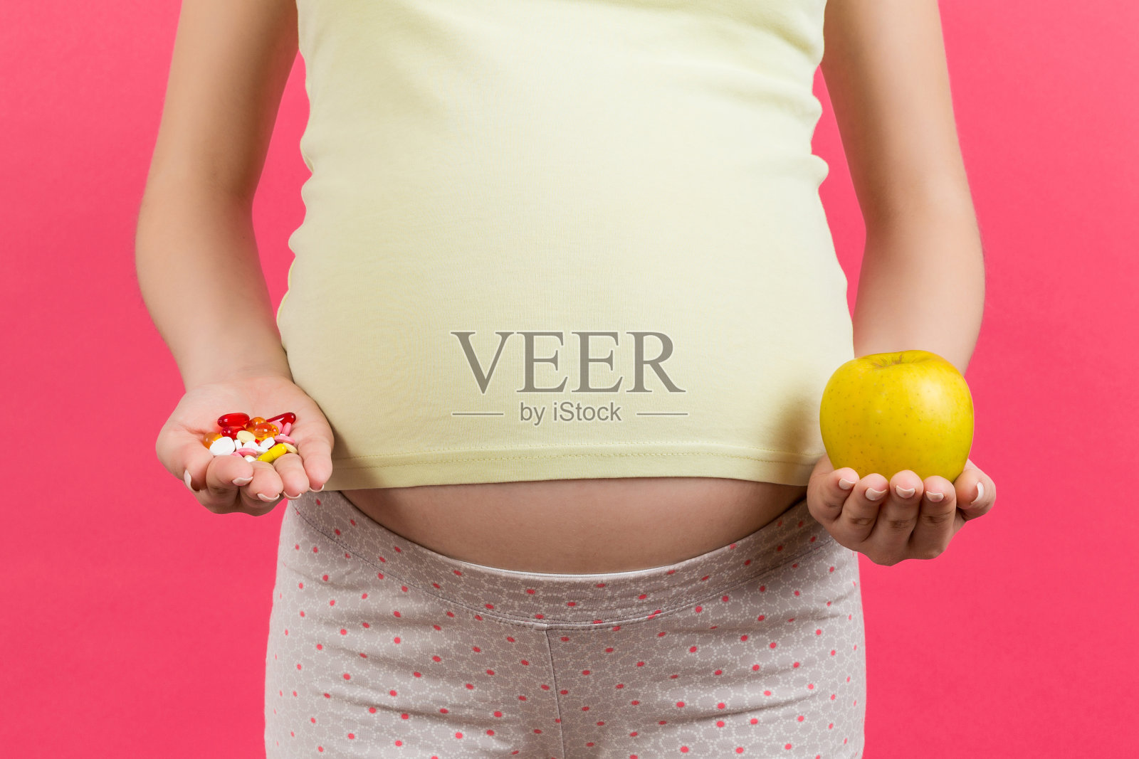 近距离的孕妇选择一个苹果和一堆药丸在彩色背景与复制空间。怀孕期间服用维生素照片摄影图片