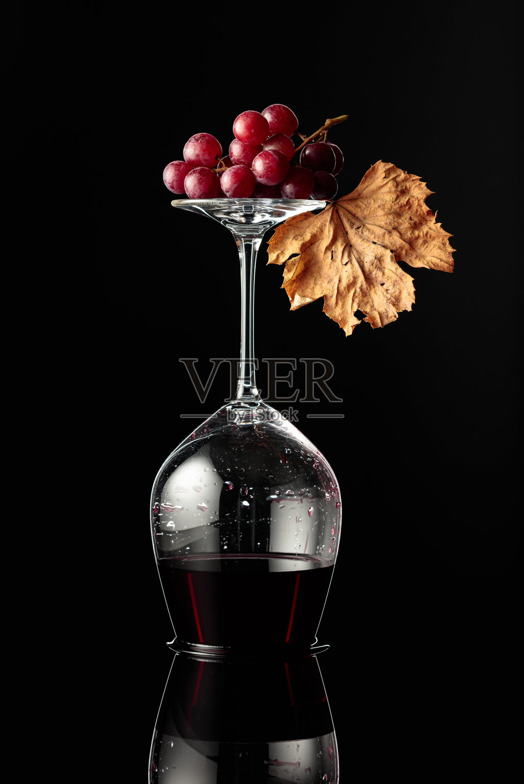 倒置的葡萄酒杯与红酒在黑色反光的背景。照片摄影图片