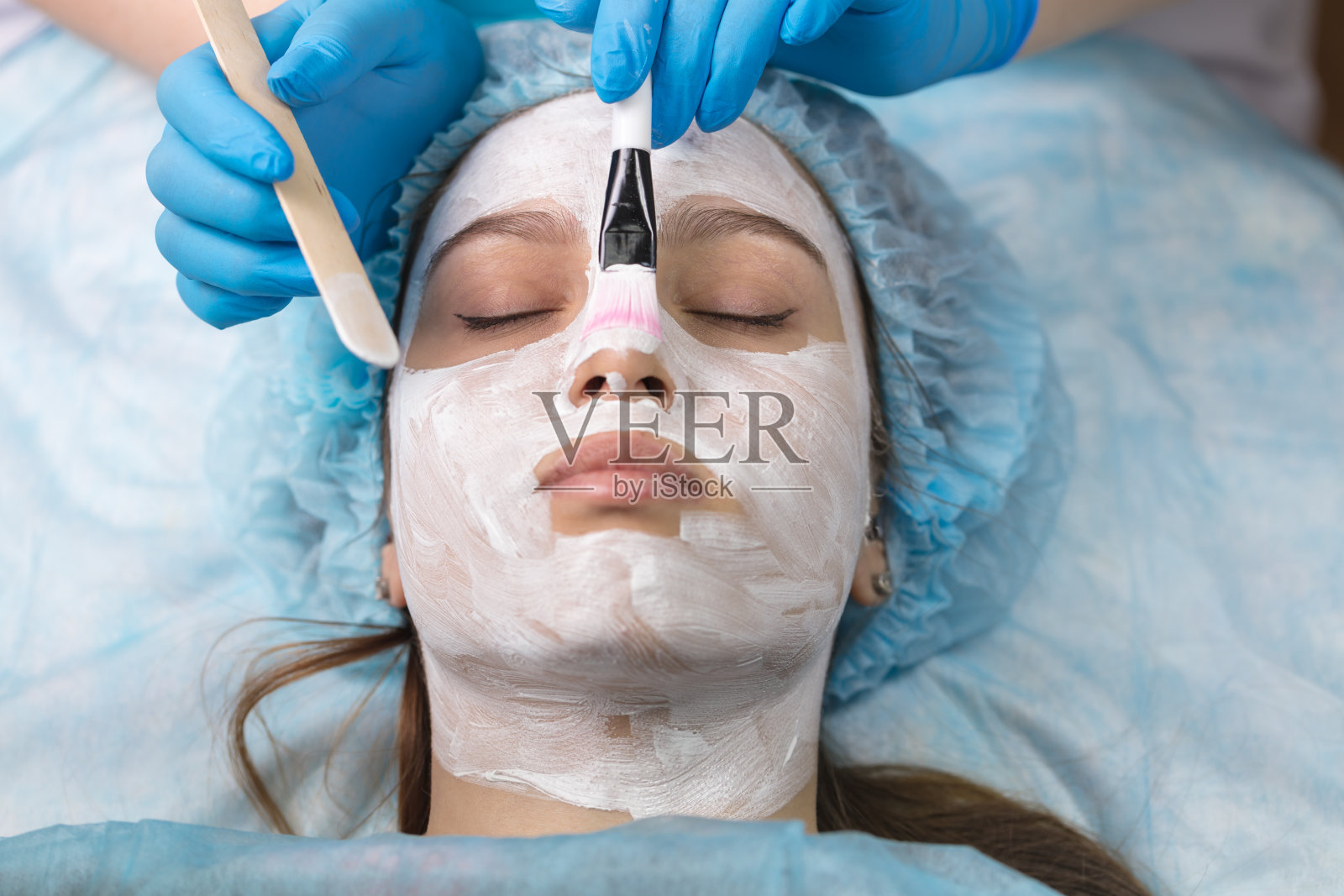 一位年轻的女士正在接受一位美容师的预约。一个漂亮的女孩戴着一个恢复活力的面具。照片摄影图片