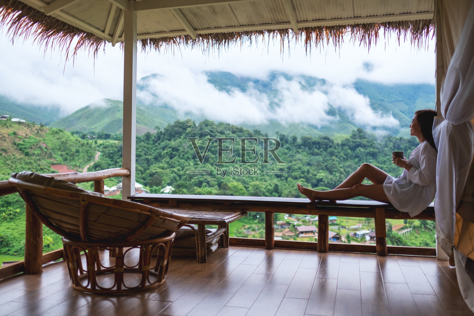 一个美丽的亚洲女人拿着并喝着热咖啡，坐在阳台上看山和绿色的自然照片摄影图片