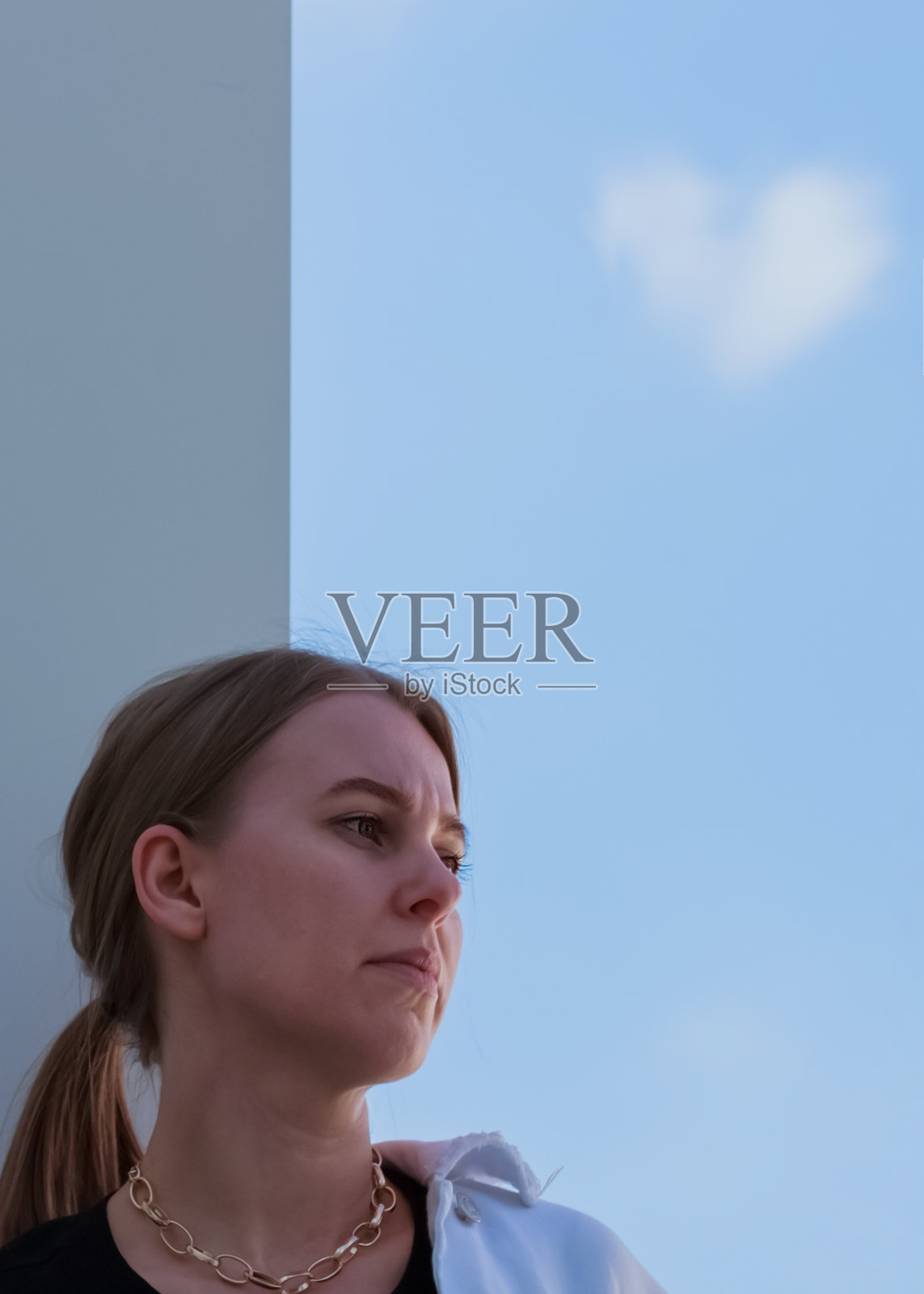 一个现代单身女孩的肖像。悲伤和遇见爱的梦想。看向一边。华尔街，蓝色的天空和心形的云。照片摄影图片