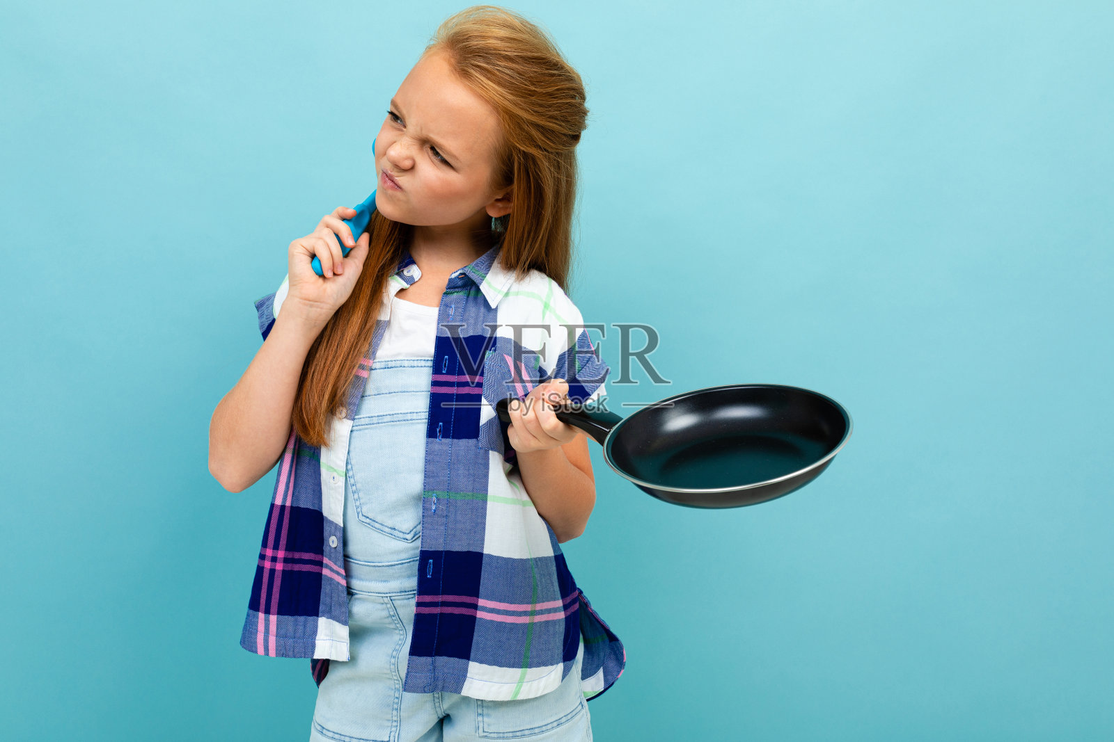 一个漂亮的欧洲女孩，手里拿着平底锅，背景是淡蓝色照片摄影图片