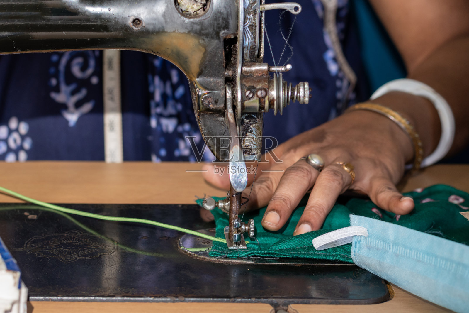 在旧缝纫机上工作的印度妇女——制作自制口罩以防止冠状病毒或新冠病毒传播，移动的针和手指拿着织物的特写细节照片摄影图片