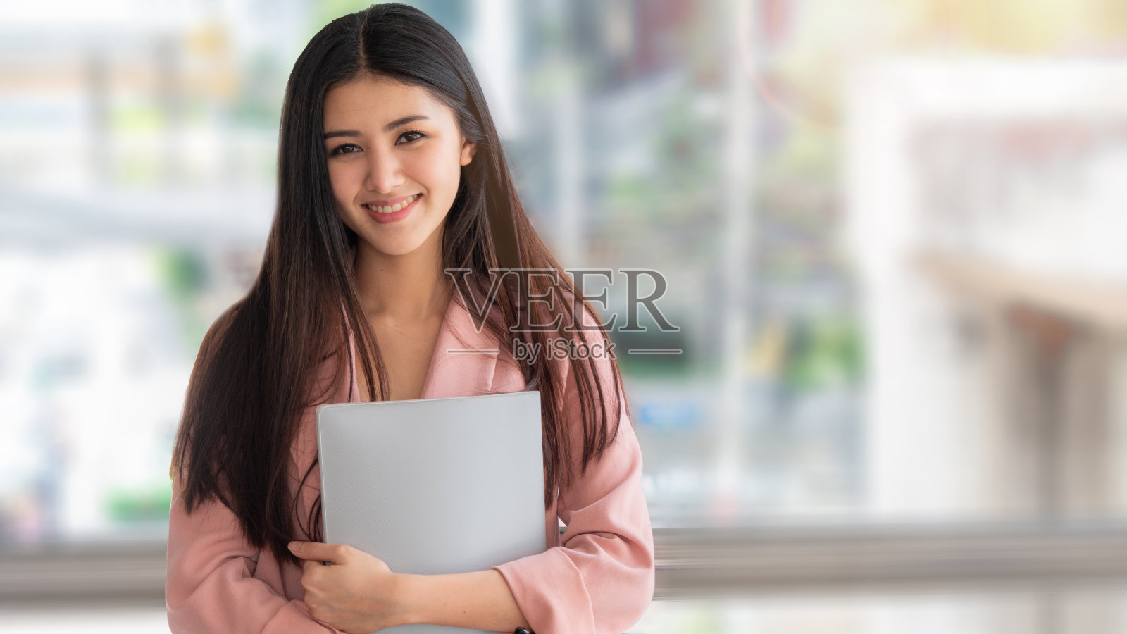 商务亚洲女性带着大大的微笑，自信地拿着文件夹。室外背景模糊。照片摄影图片