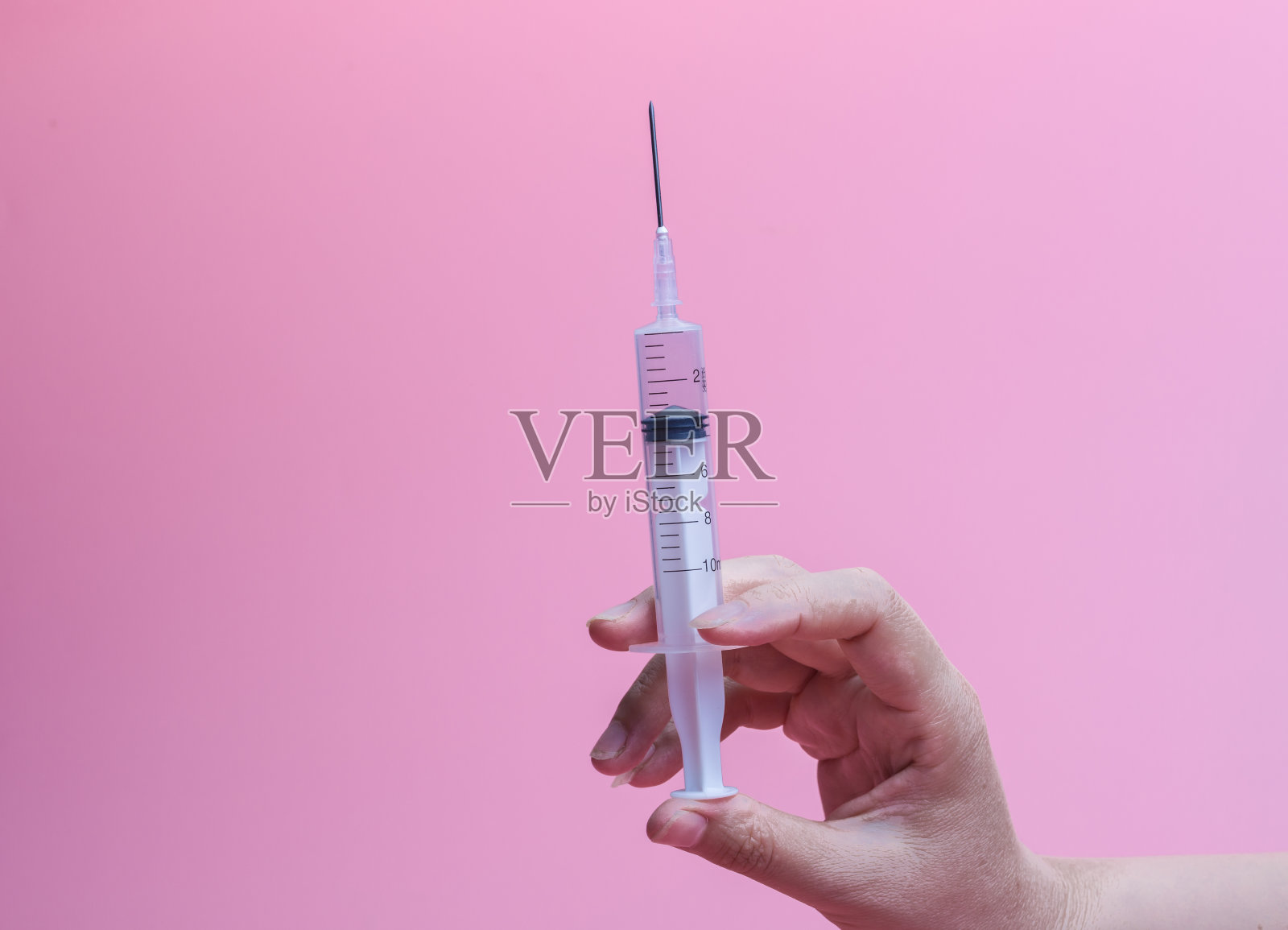 手持注射器在粉红色的背景照片摄影图片