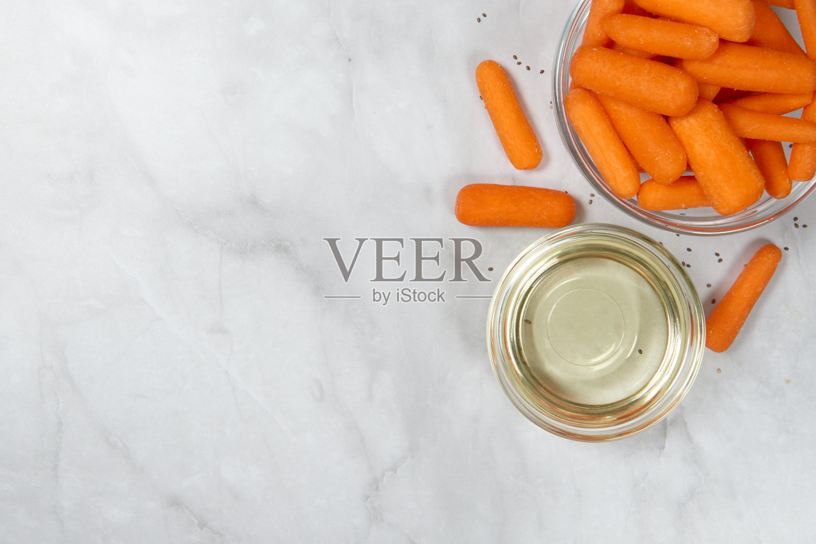 新鲜生的去皮小胡萝卜准备在玻璃碗和油在大理石背景上吃。健康零食、有机食品及饮食理念。俯视图，关闭，复制空间。照片摄影图片