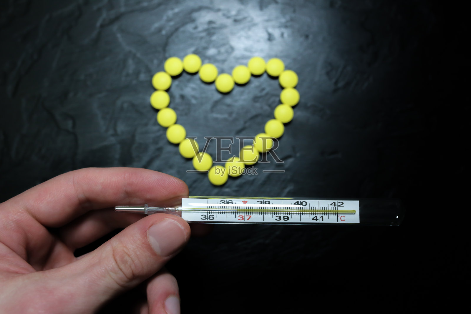 男子手持36.6度的水银温度计。健康的人。背景上心脏形状的药丸。健康的心血管系统。照片摄影图片