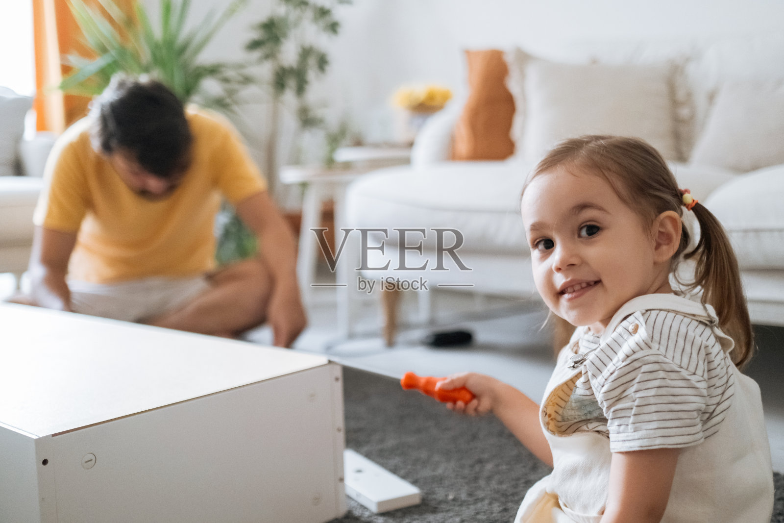 在他们的起居室里，小女孩在他父亲的帮助下试图组装家具照片摄影图片