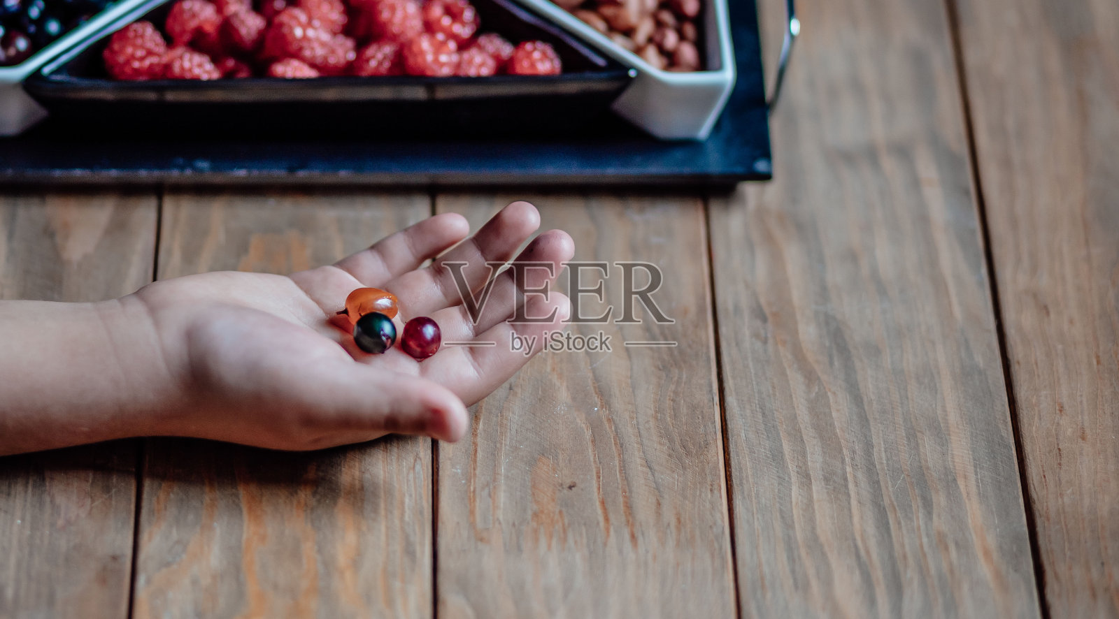 孩子在木桌上用手掌捧着浆果。桌上放着装着覆盆子和醋栗的花瓶照片摄影图片
