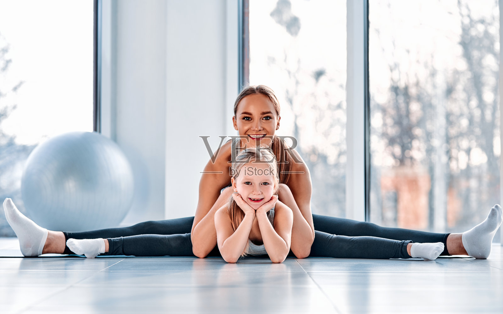 所以灵活。一名年轻女子在做劈叉时坐在女儿后面照片摄影图片