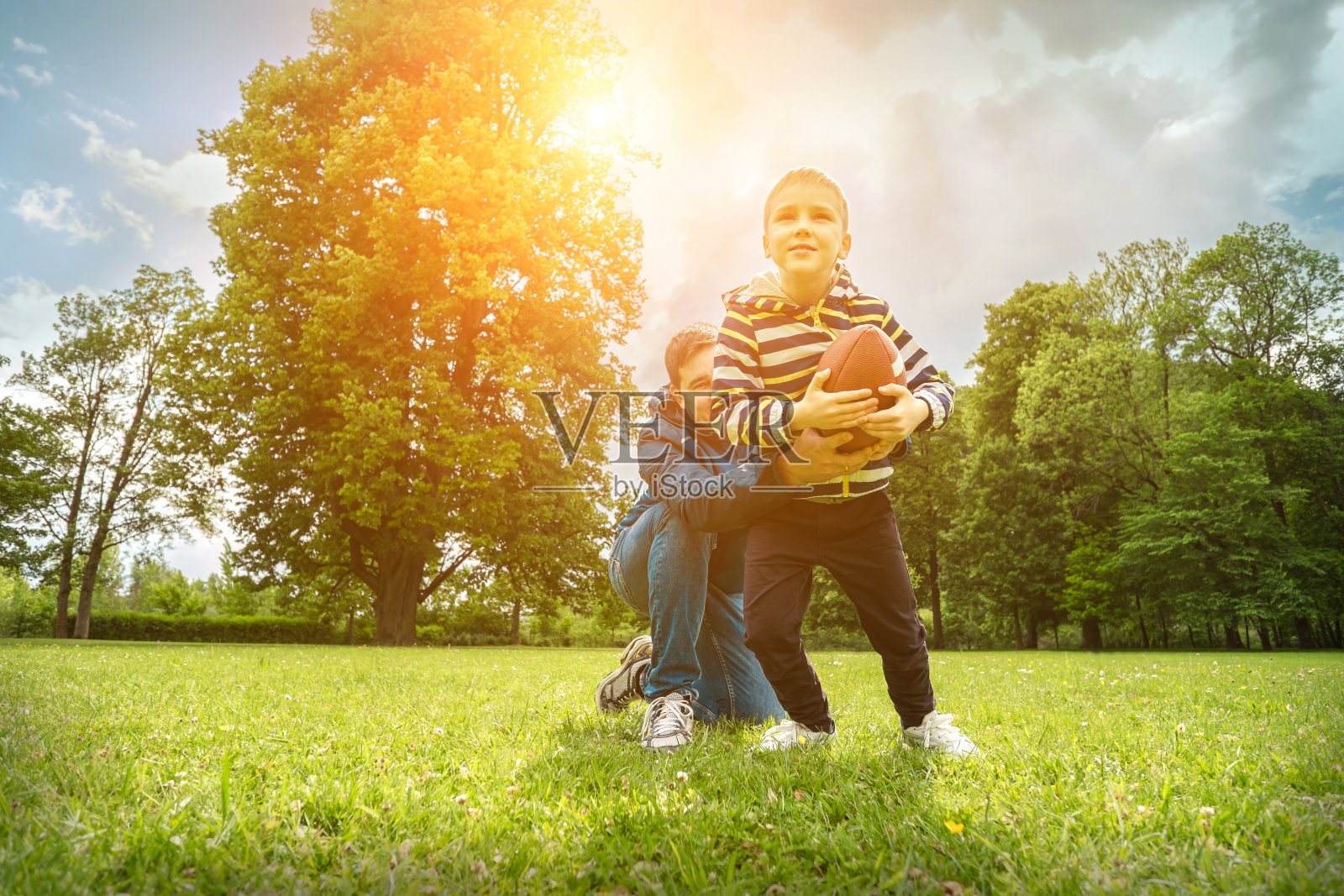 父亲和儿子在踢足球，父亲节，爱玩的男人教男孩橄榄球户外在阳光明媚的一天在公园。家庭体育的周末。照片摄影图片