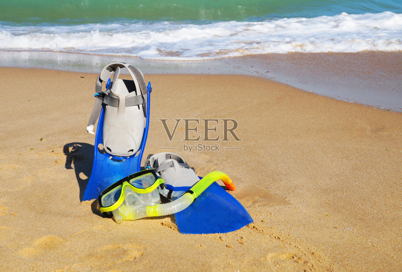 鳍状肢和面具为游泳在沙滩上对抗大海和晴朗的天空的背景照片摄影图片