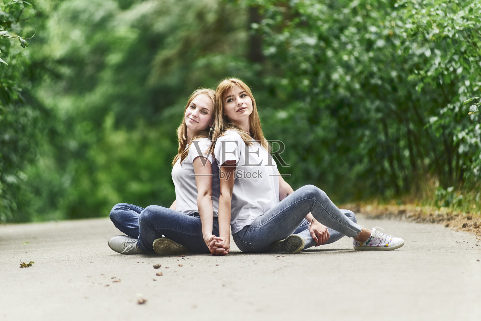 两个年轻女人背靠背坐在公园的路上照片摄影图片