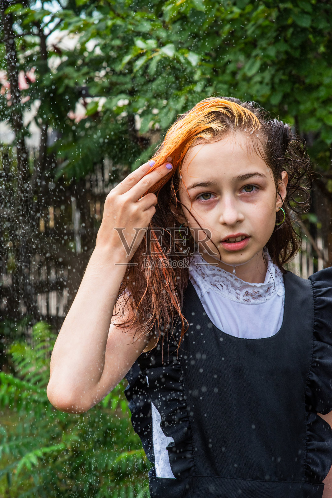 湿漉漉的女生站在雨中。少年在春天或温暖的秋天穿着校服。五年级的女孩。染发。照片摄影图片