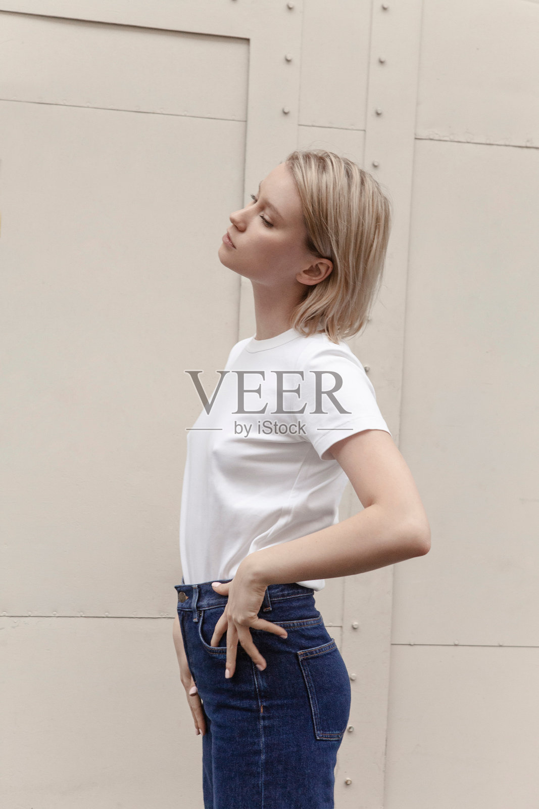 美丽年轻的金发女人短发白色t恤和蓝色牛仔裤在米色背景时尚模特户外肖像街风格照片摄影图片