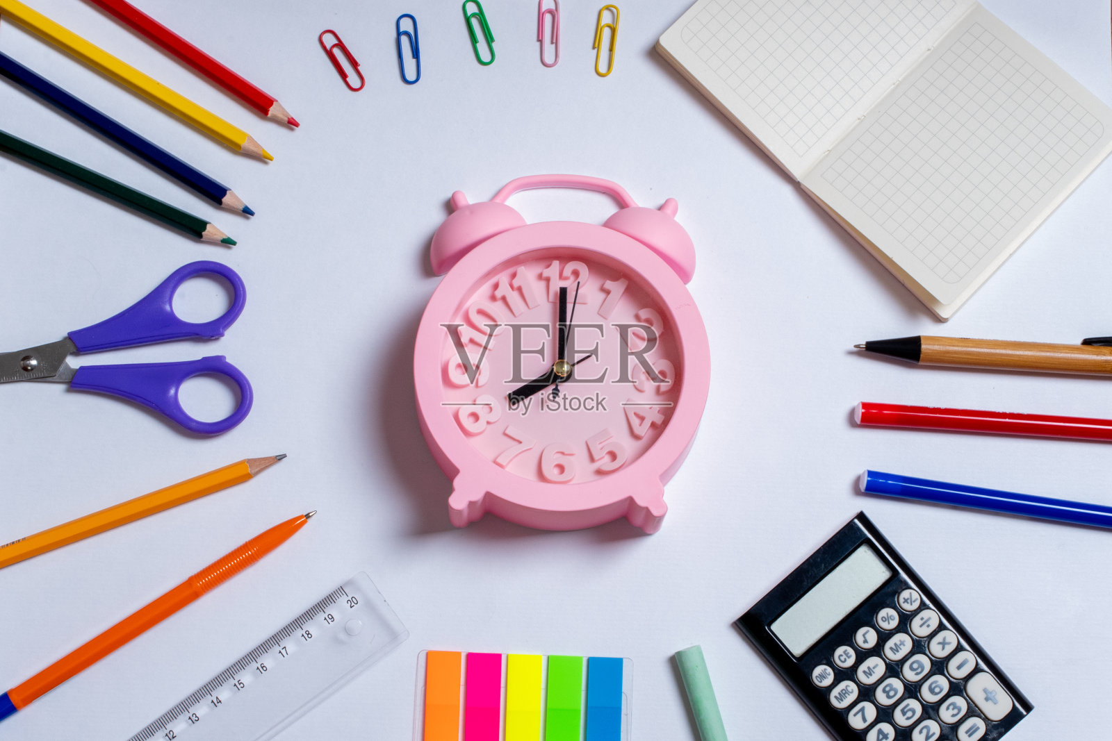 创意平铺顶视图回校理念。彩色的学习用品和白色背景的粉色闹钟照片摄影图片