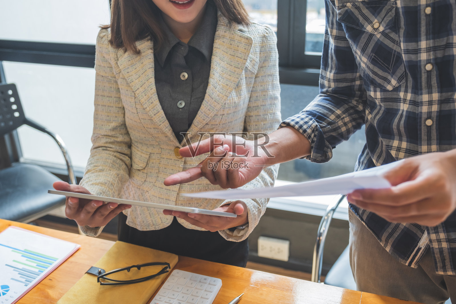 在比较财务报告和平板电脑上的数字时，男性亚洲主管给年轻快乐的女同事提供建议。照片摄影图片