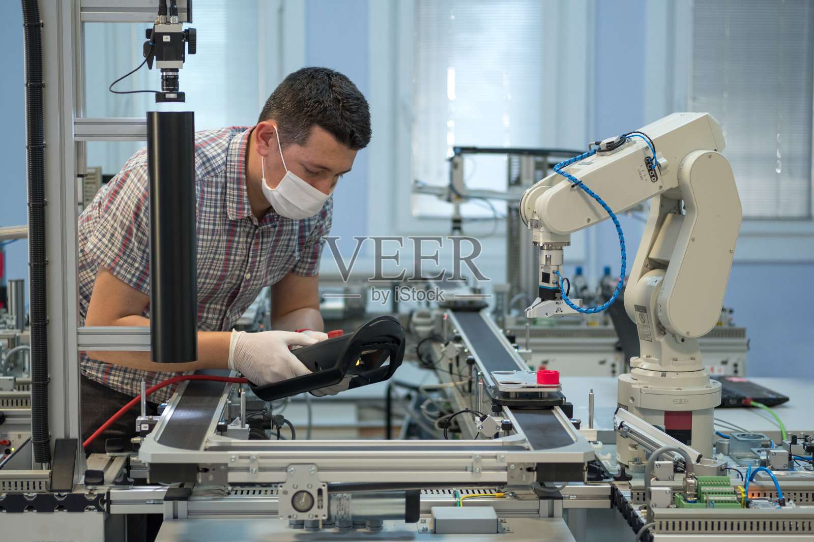 工业4.0:带手术口罩和手套的人防COVID-19(冠状病毒)编程机器人手臂和教学吊坠。照片摄影图片