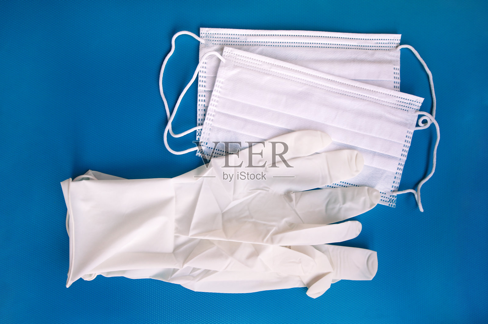 医用防护一次性白色口罩和手套，蓝色背景。预防病毒、流感和冠状病毒(COVID-19)、细菌和细菌的防护设备。保健和外科概念。照片摄影图片