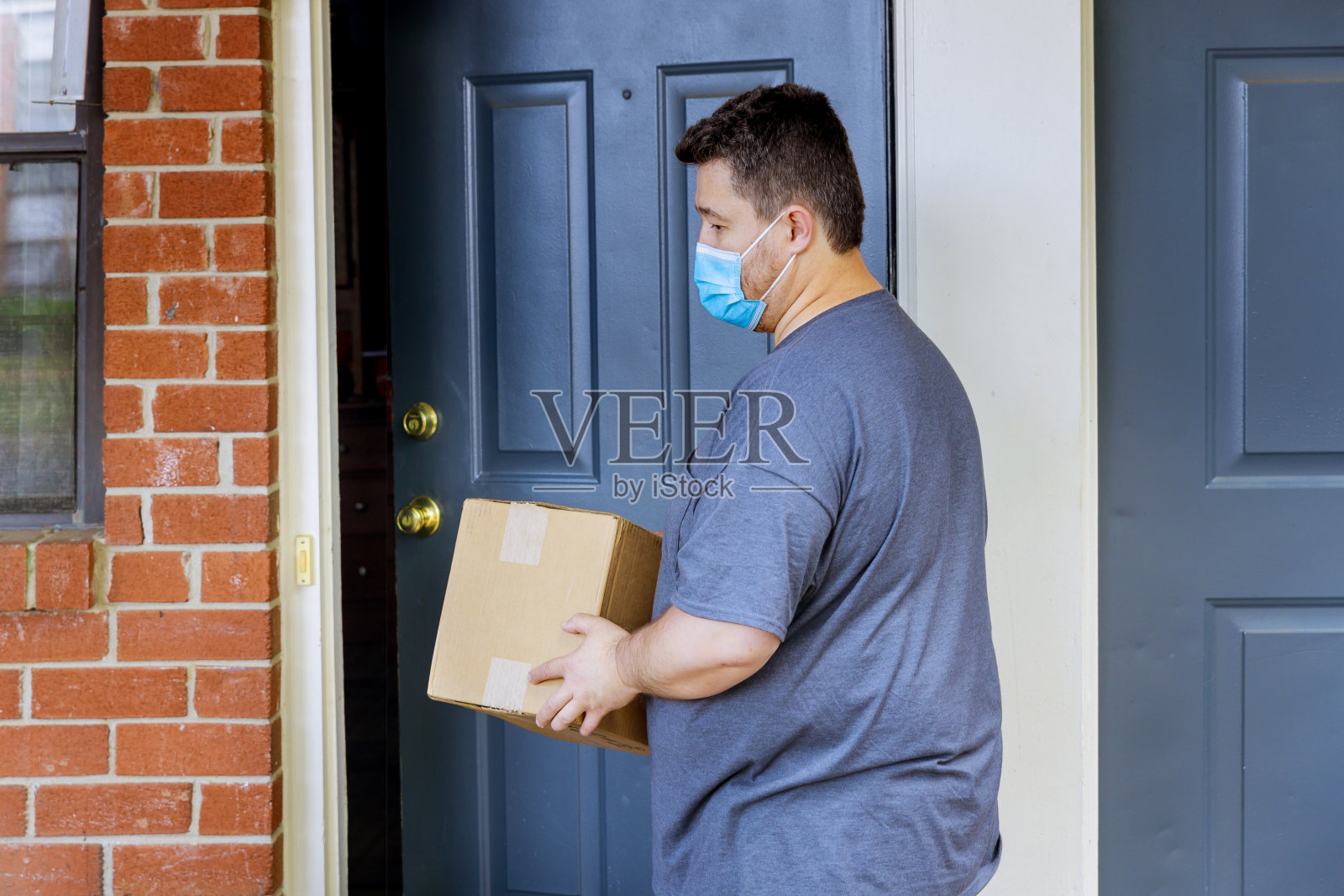 在冠状病毒大流行隔离期间，一名男子带着医用口罩，手里拿着一个盒子包裹照片摄影图片