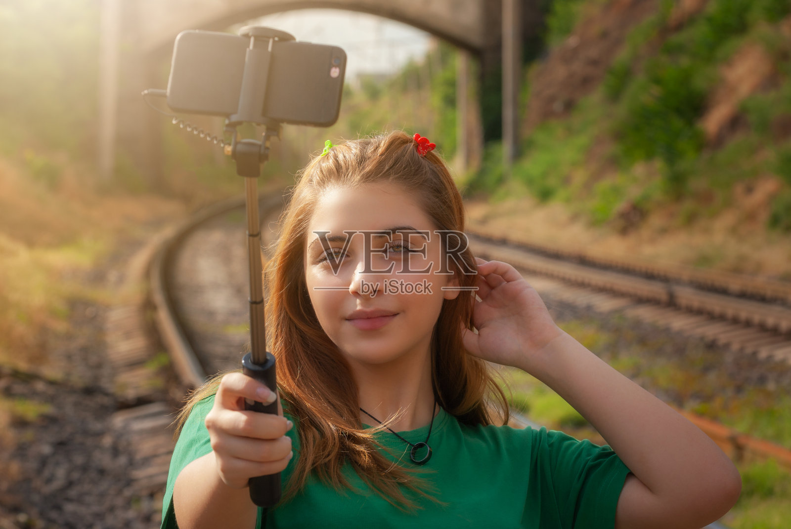 一个美丽的十几岁的女孩的近距离肖像手机摆姿势在火车轨道上照片摄影图片