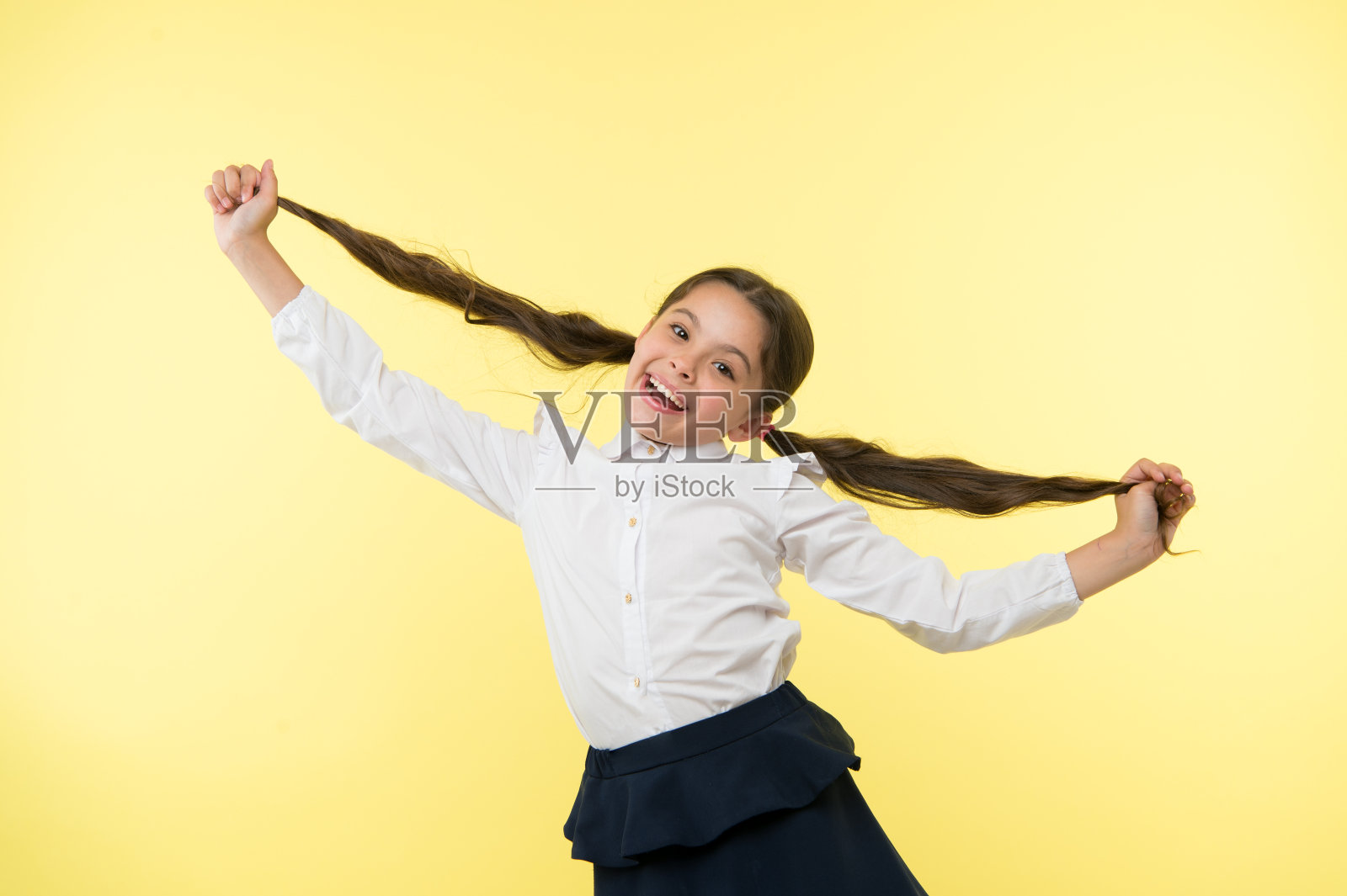 快乐的女孩在黄色的背景上展示了长长的黑发。小孩笑着换了新发型。理发师沙龙服务。为她美丽的头发感到骄傲。美容院。时尚和可爱照片摄影图片