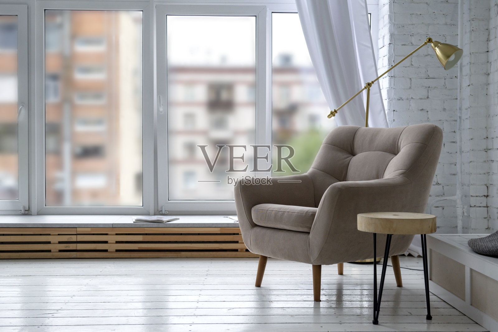 室内光线充足，白色木地板上放着一把米色扶手椅，窗户的背景上放着一盏灯照片摄影图片