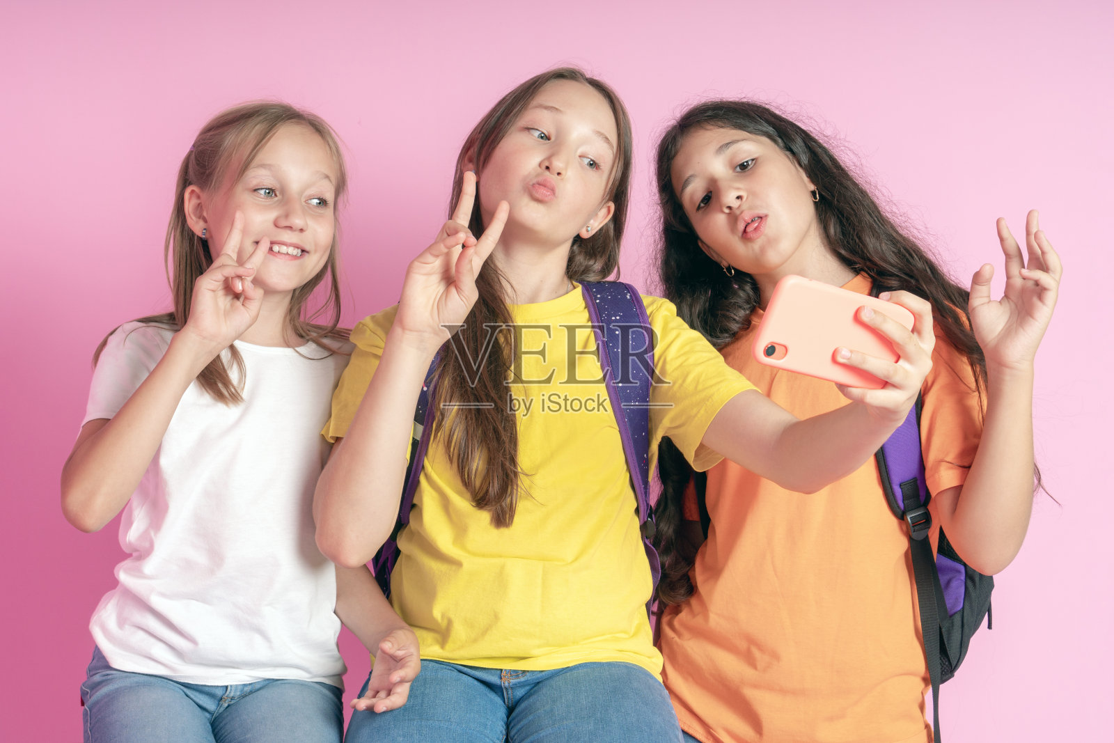 三个十几岁的女孩微笑着拍了一段粉色背景的视频。Selfies照片摄影图片