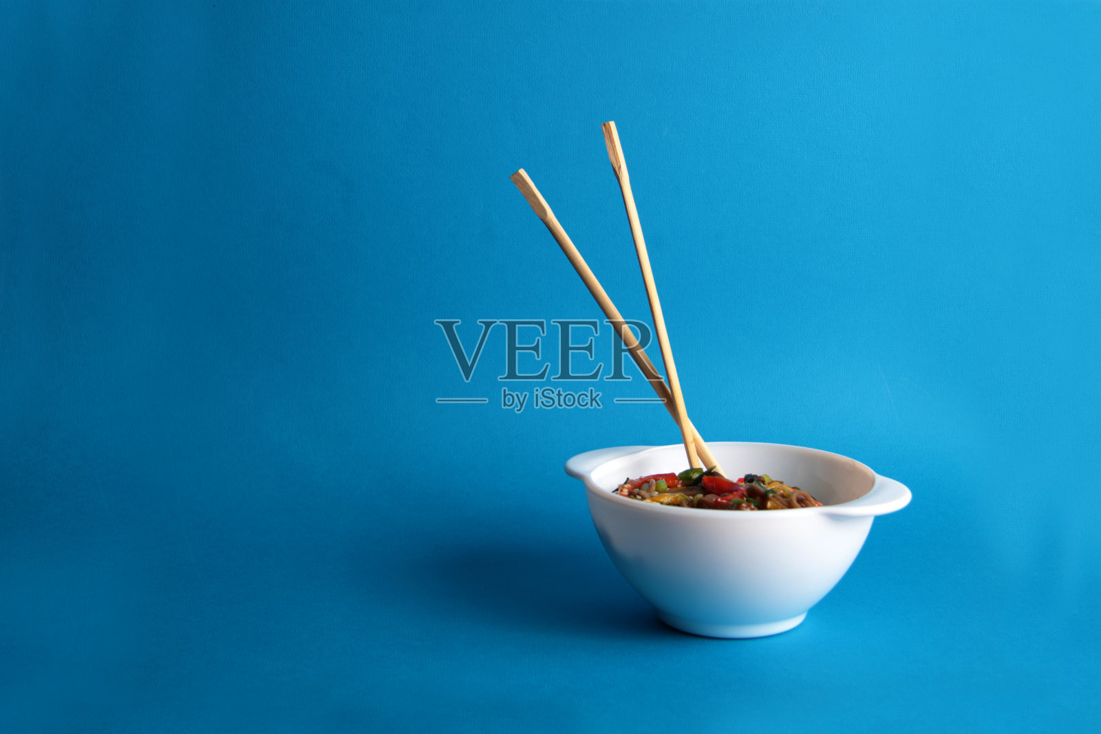 一碗炒面和筷子孤立在蓝色背景上照片摄影图片