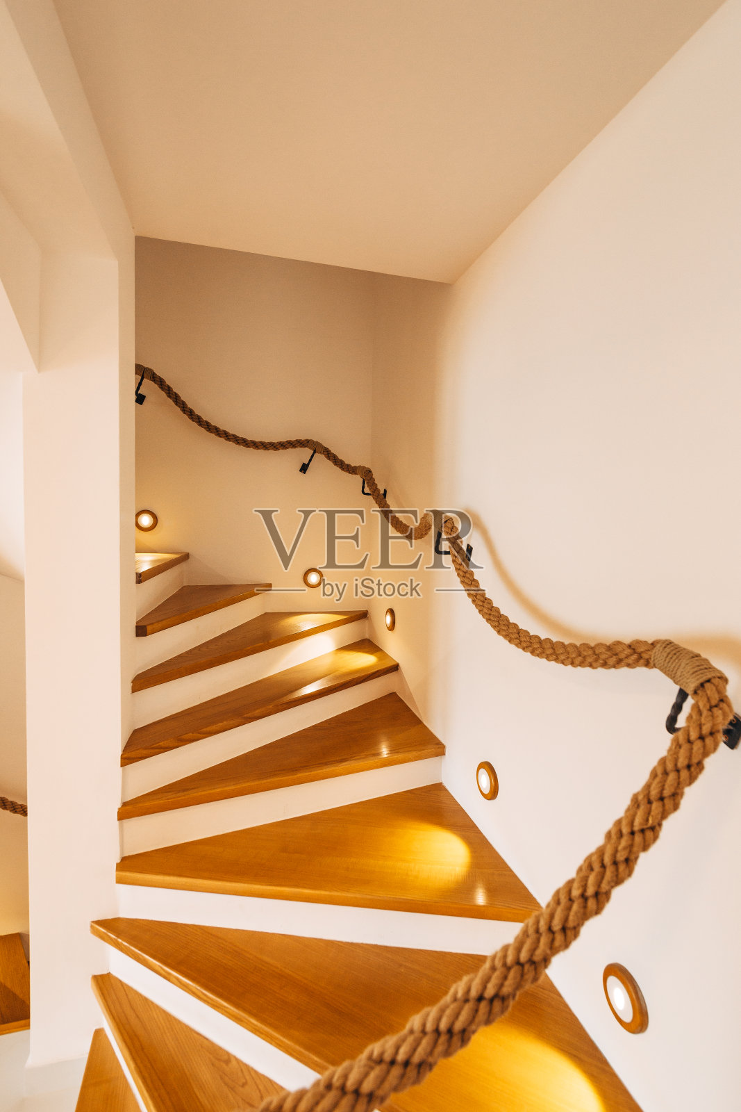白色墙壁的房子里有照明的台阶和绳索栏杆的楼梯。照片摄影图片