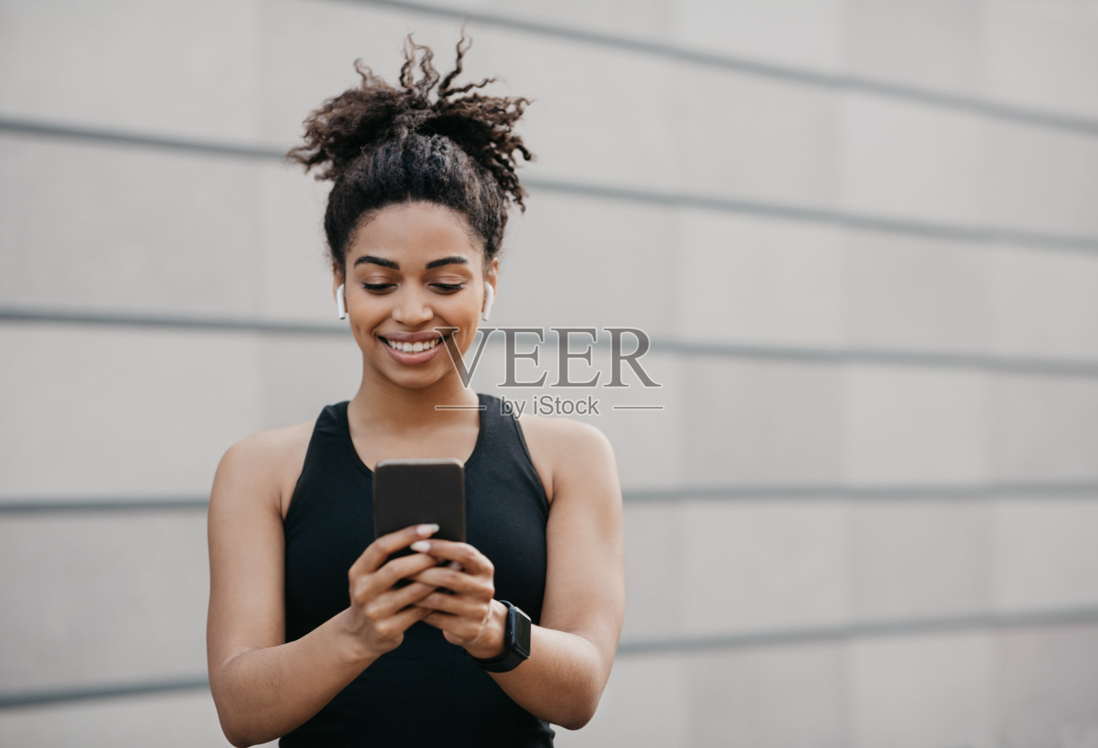 好心情，音乐和运动。快乐的非裔美国运动女孩在运动服装与健身追踪器使用智能手机照片摄影图片