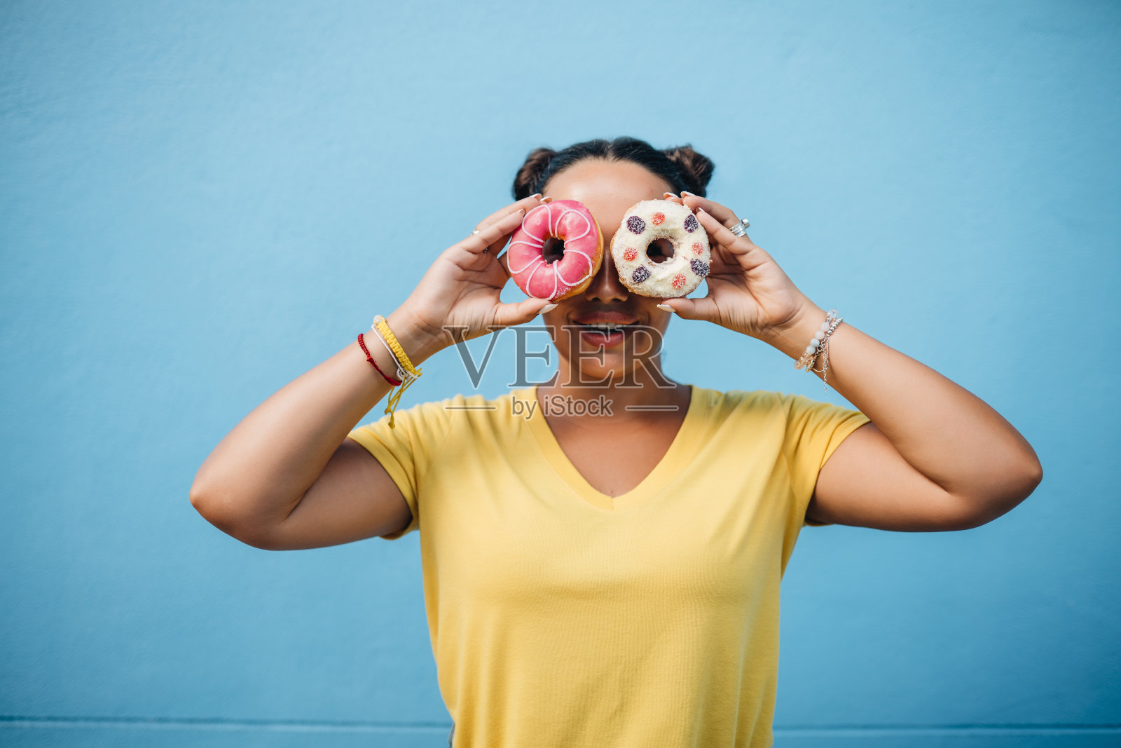 一个穿着黄色t恤的女孩在蓝墙吃甜甜圈的肖像照片摄影图片