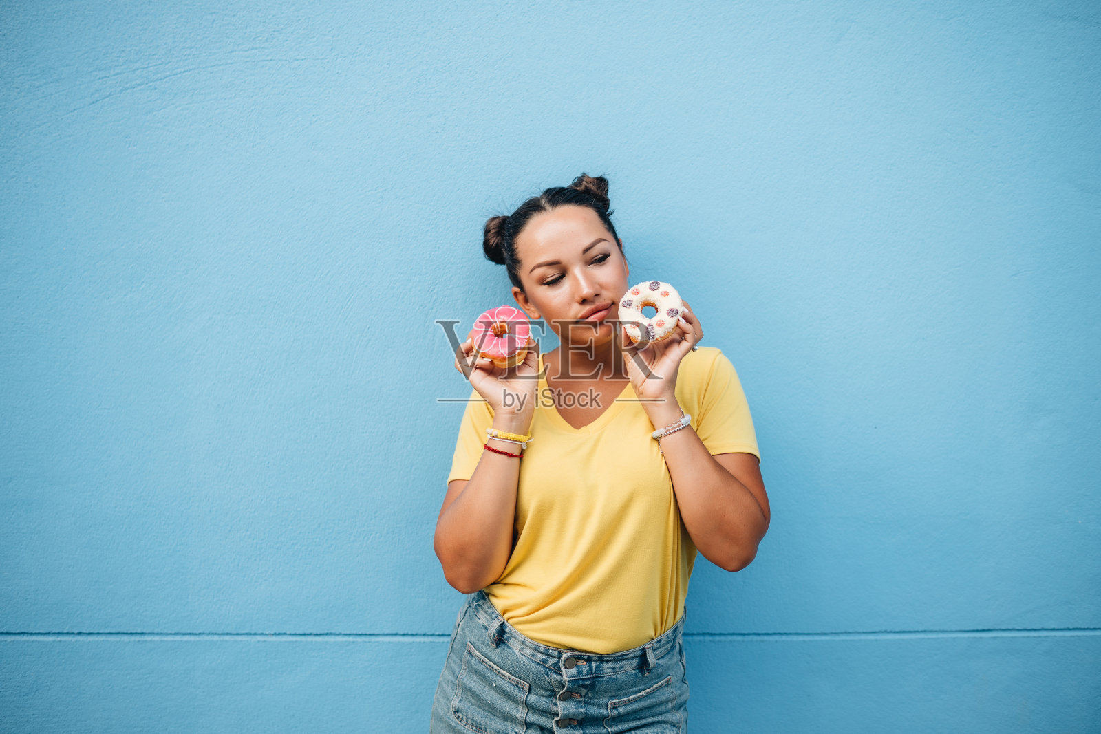 一个穿着黄色t恤的女孩在蓝墙吃甜甜圈的肖像照片摄影图片