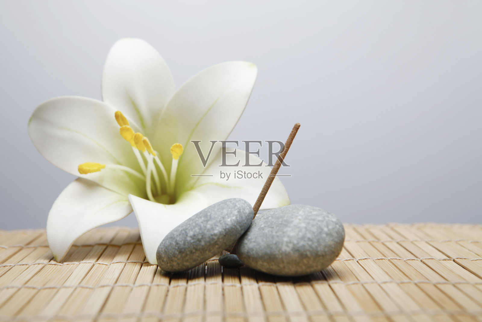 在鹅卵石中间放一根香，背景上放一朵花照片摄影图片