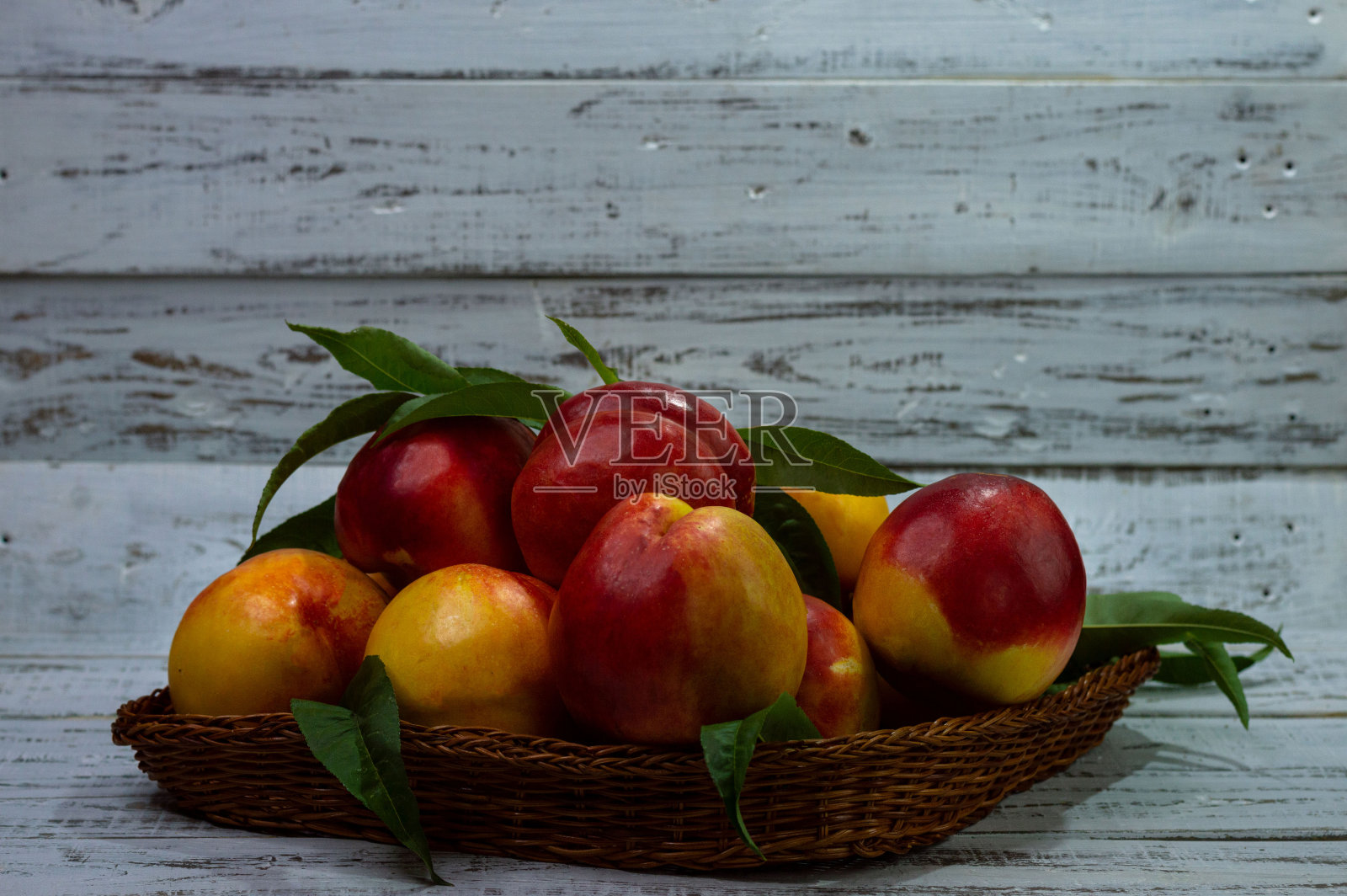篮子里装着成熟的桃子，放在白色的木制背景上。夏天。桃子丰收。身体所需的维生素。明亮的结构背景。照片摄影图片