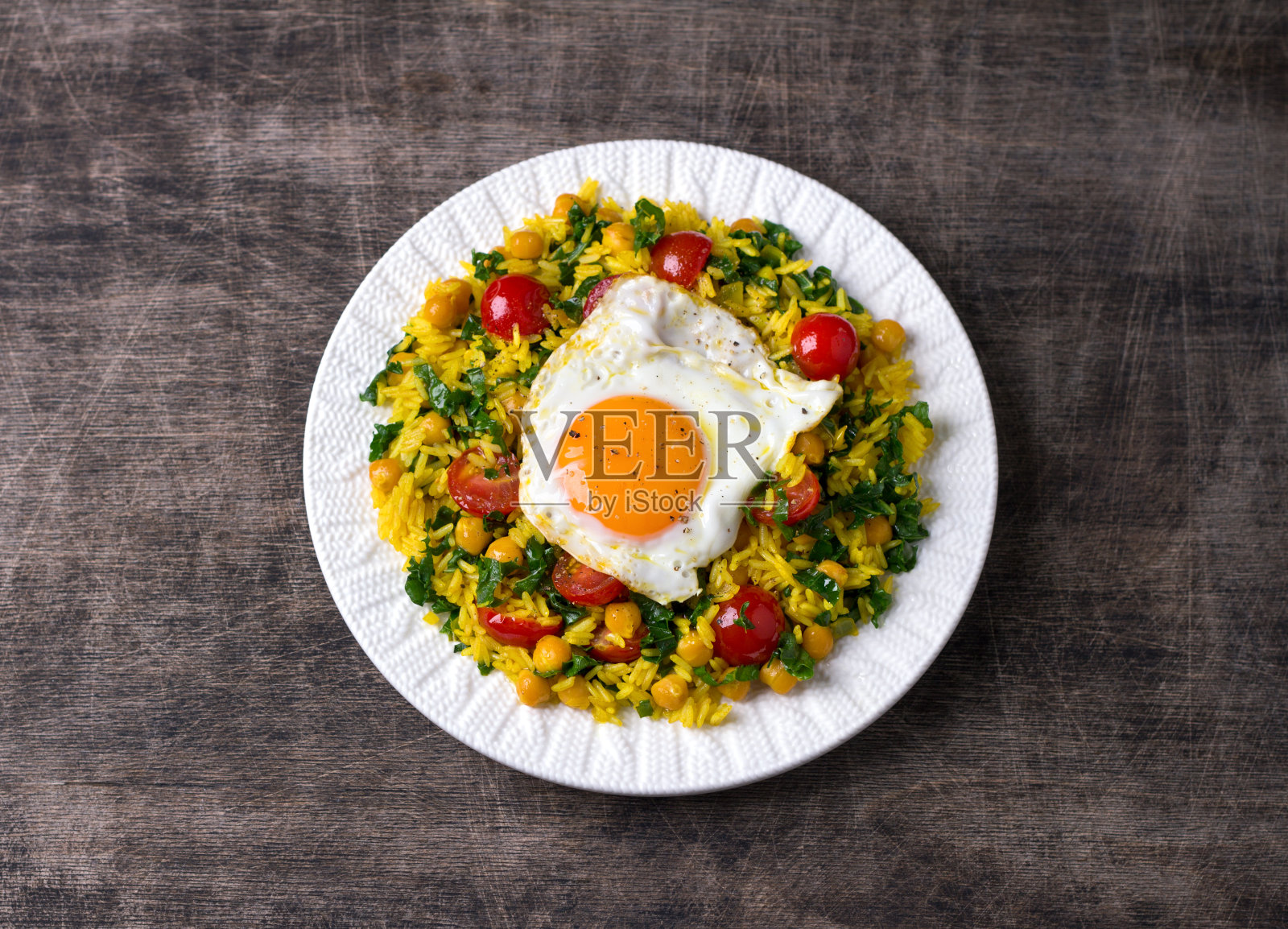 中式炒饭，以姜黄、鹰嘴豆、番茄、羽衣甘蓝和炒鸡蛋为背景，放在白色陶瓷盘子上照片摄影图片