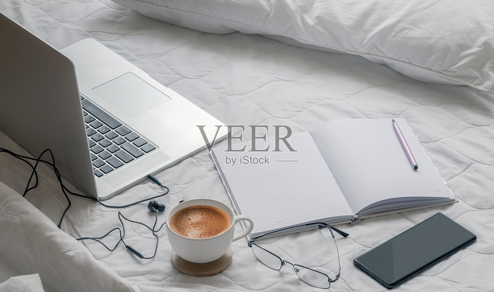 用笔记本电脑在家工作，在卧室里铺上白色的床单。照片摄影图片