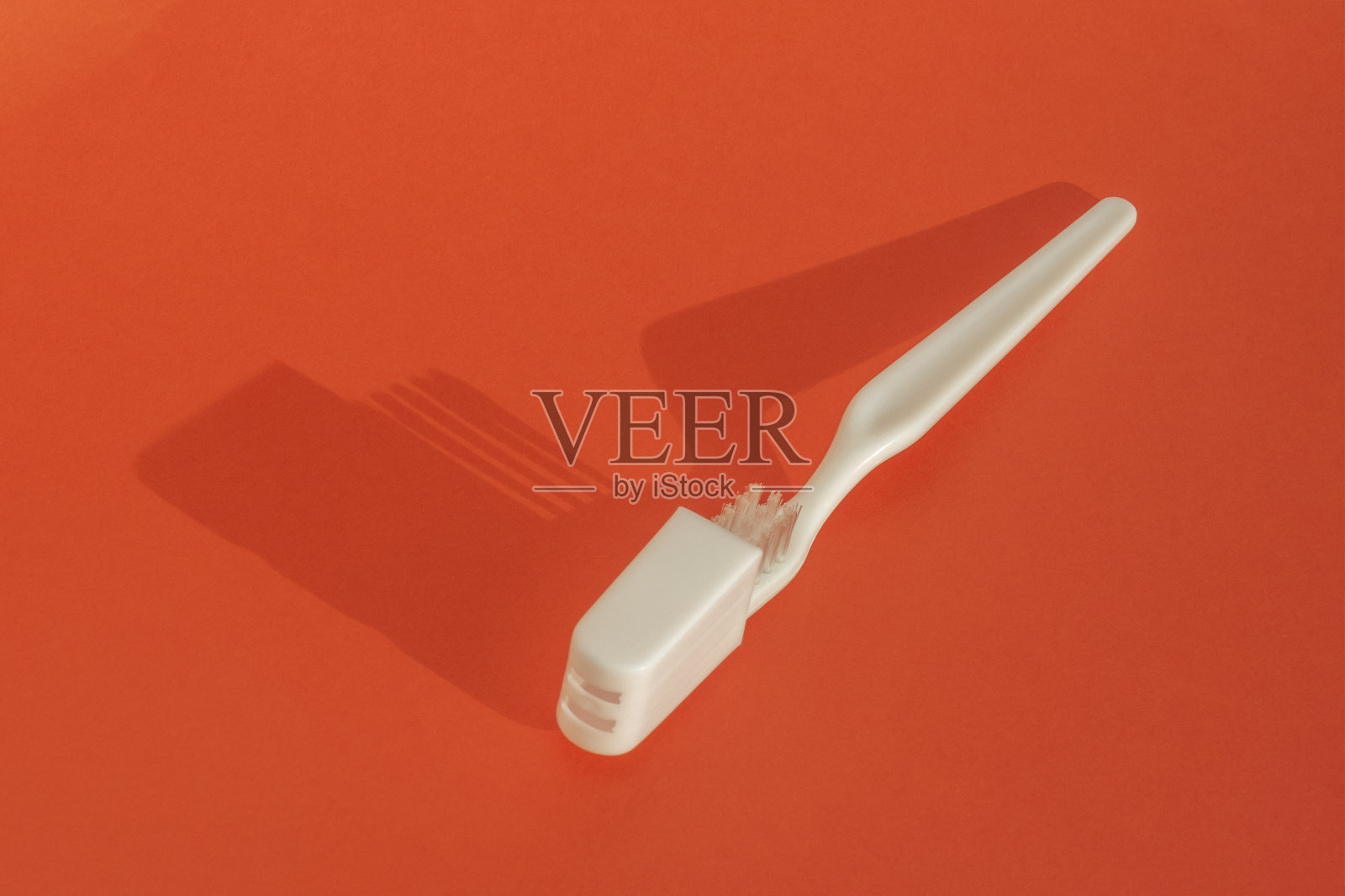 白色的牙刷半隐藏在白色的塑料盒和阴影在红色的背景。照片摄影图片