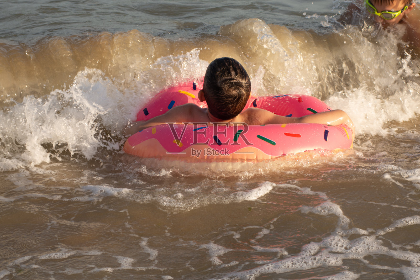 一个快乐的5岁男孩在阳光明媚的日子里，骑着一个甜甜圈形状的充气圈在海里游泳。照片摄影图片