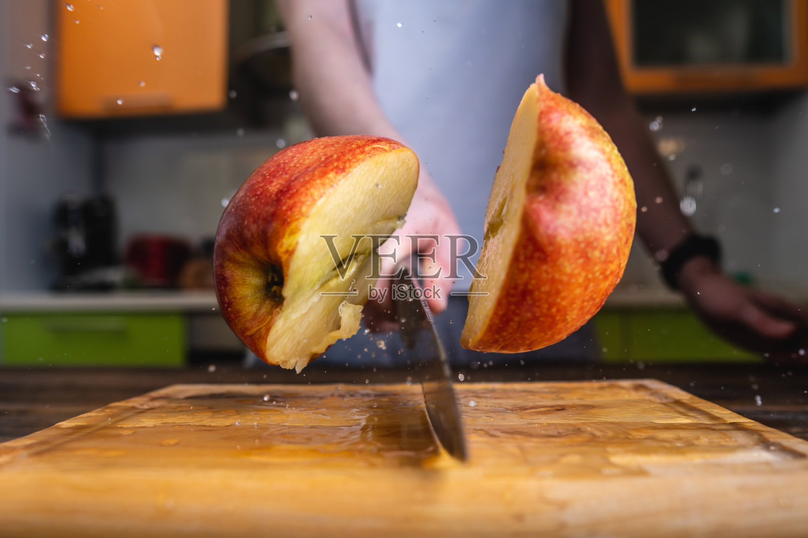 厨师用刀将熟苹果切成两半。水和果汁飞溅到不同的方向照片摄影图片