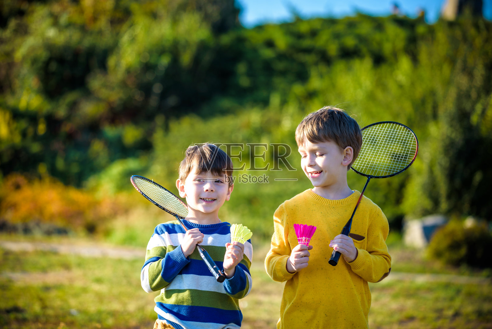 活泼的幼稚园女孩和男孩在户外球场打羽毛球在夏天。孩子们打网球。孩子们的学校运动。球拍和羽毛球运动的儿童运动员。照片摄影图片